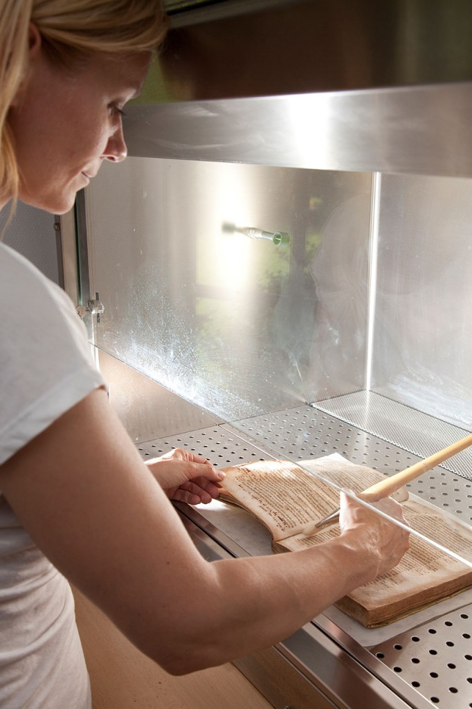 Papierrestauratorin bei der mechanischen Schimmelreinigung an einer reinen Werkbank mit professioneller Absaugung